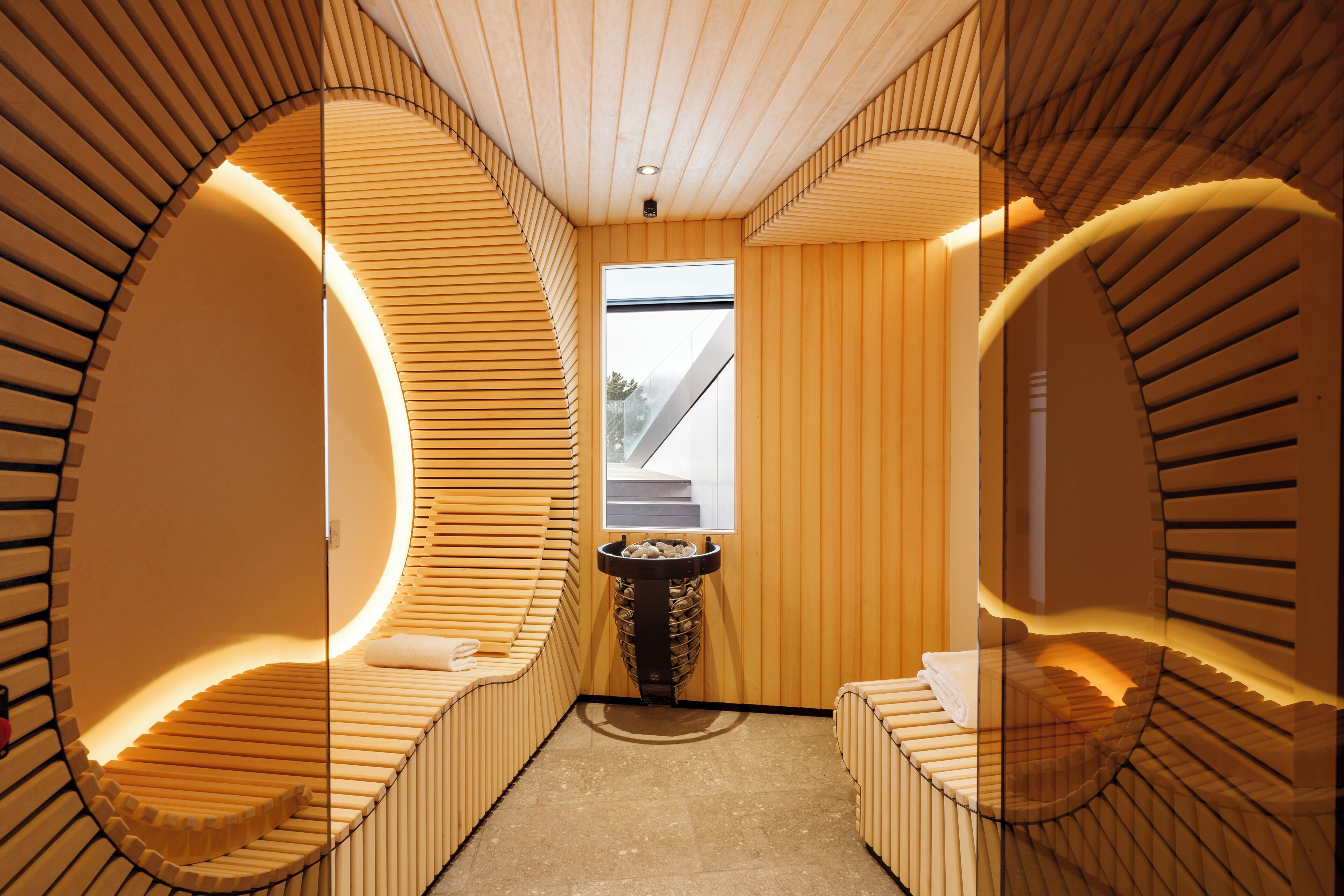 Ein moderner Wellnessraum mit Holzschubwänden, einem zentralen Waschbecken und Blick ins Freie.