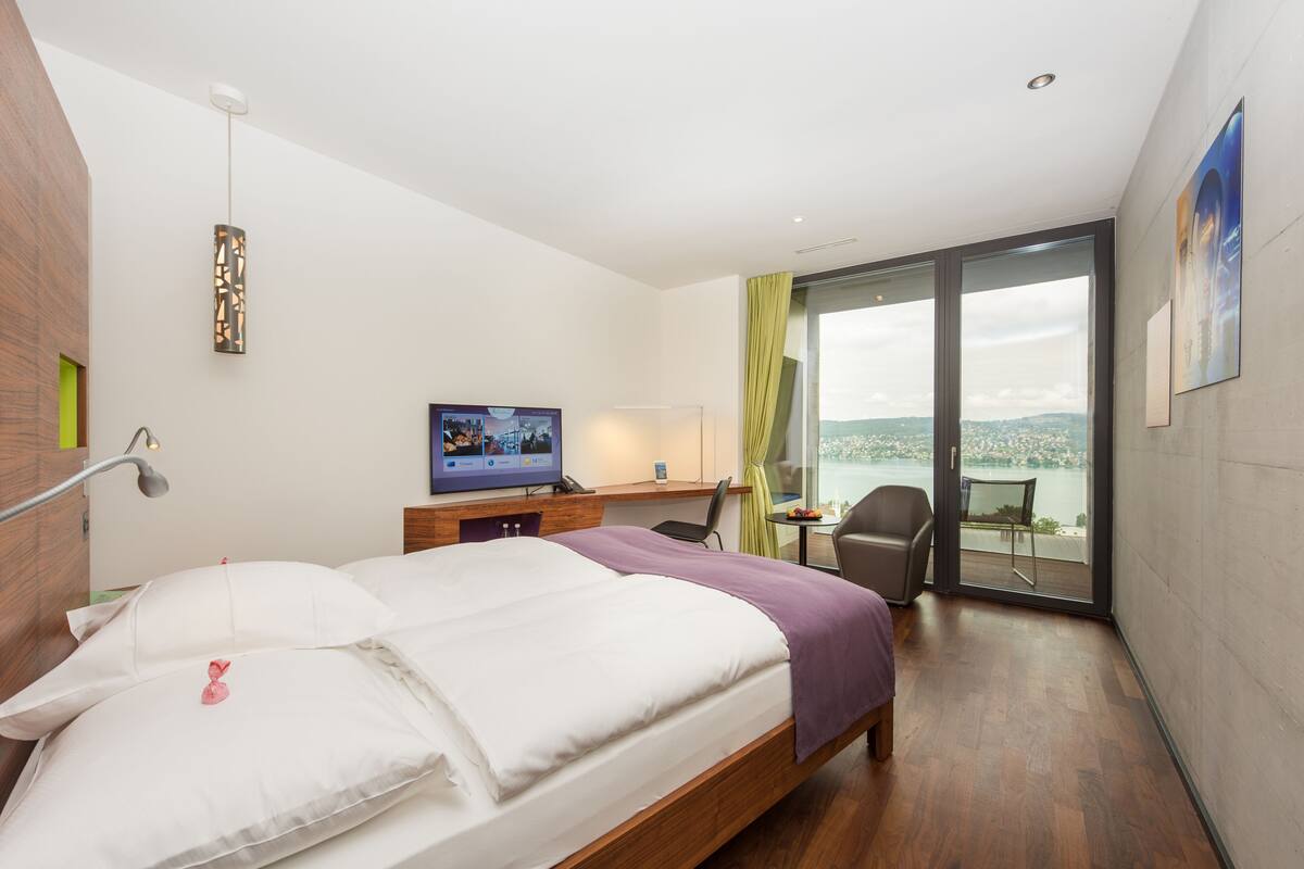 Ein Hotelzimmer mit Bett, Schreibtisch, Stuhl, Fernseher und einem Balkon mit Blick.