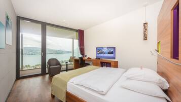 A hotel room with a bed, desk, chair, TV, and a large window with a view of the outdoors.