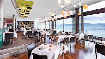A restaurant with tables set for dining, large windows offering a city view, and hanging spherical light fixtures.