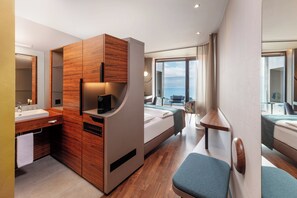 A modern hotel room with a wooden wardrobe, a built-in desk, a bed, a small table, and a large window offering a city view. - Hotel Belvoir Lake View & Spa (Rüschlikon)