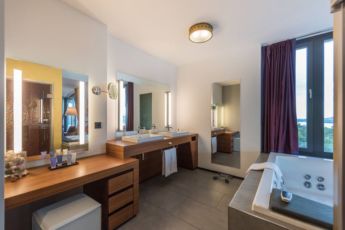 Ein modernes Badezimmer mit zwei Waschbecken, einem großen Spiegel, einer Badewanne und Blick ins Freie.