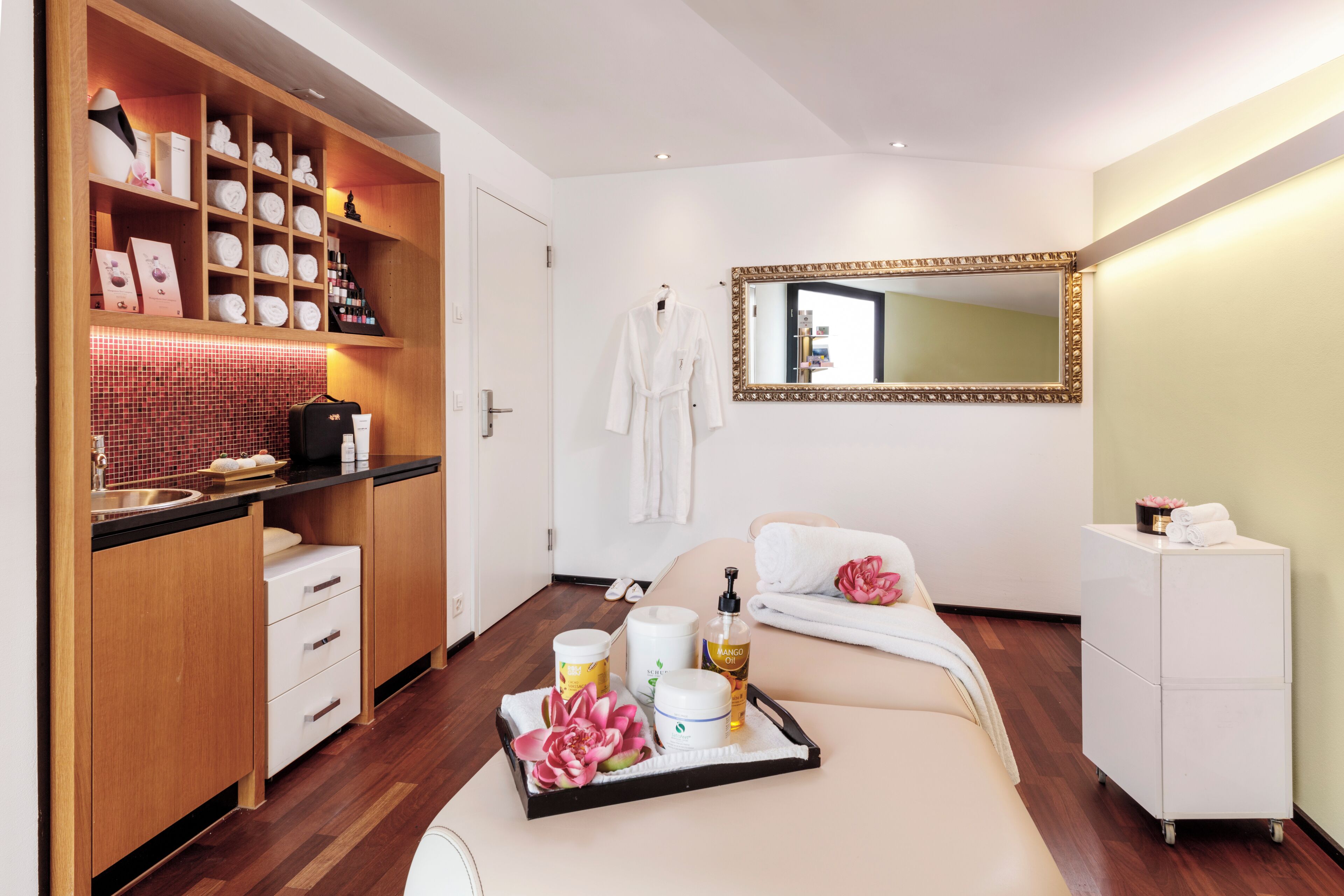 A hotel room with a wooden vanity, a large mirror, a bed with a white comforter, and a tray with toiletries.