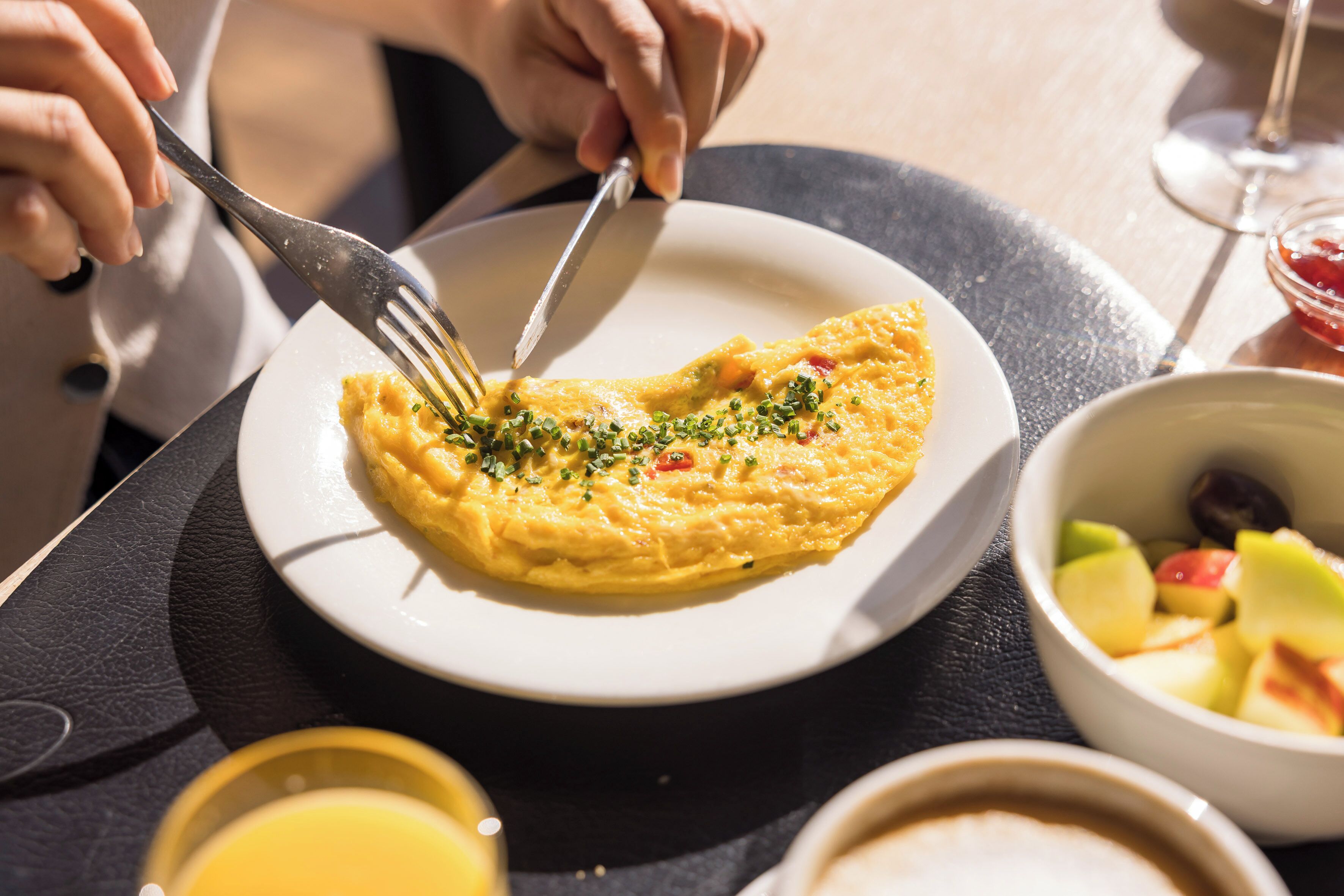 A breakfast setting with an omelette on a plate, a glass of orange juice, and a bowl of fruit.