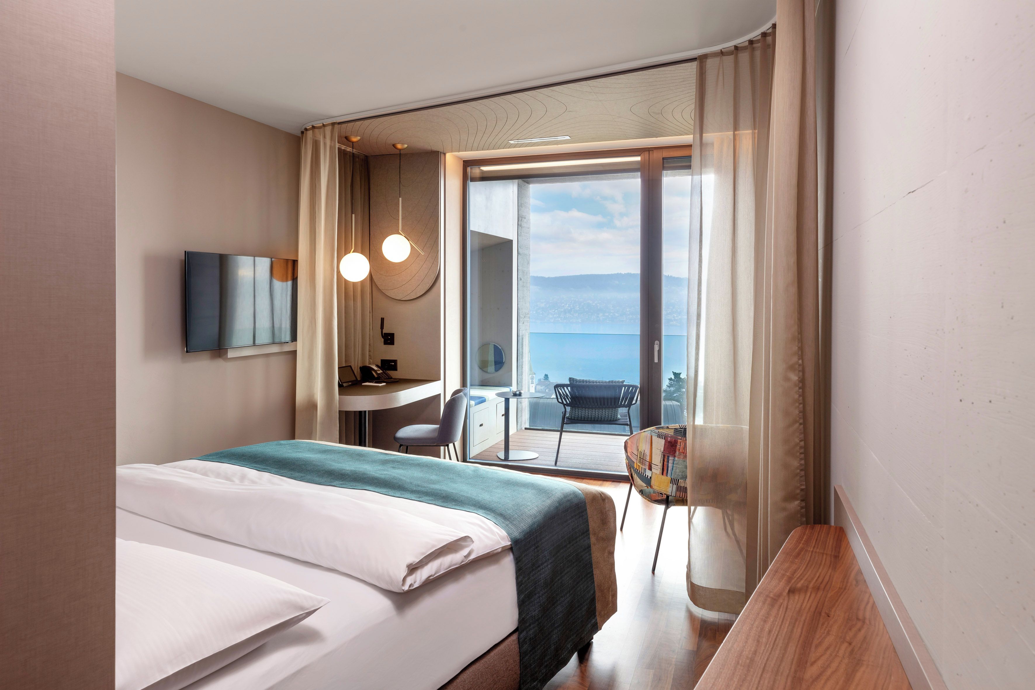 A hotel room with a bed, a desk, a chair, and a view of the sea.