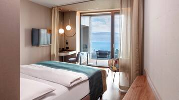 A hotel room with a bed, a desk, a chair, and a view of the sea.