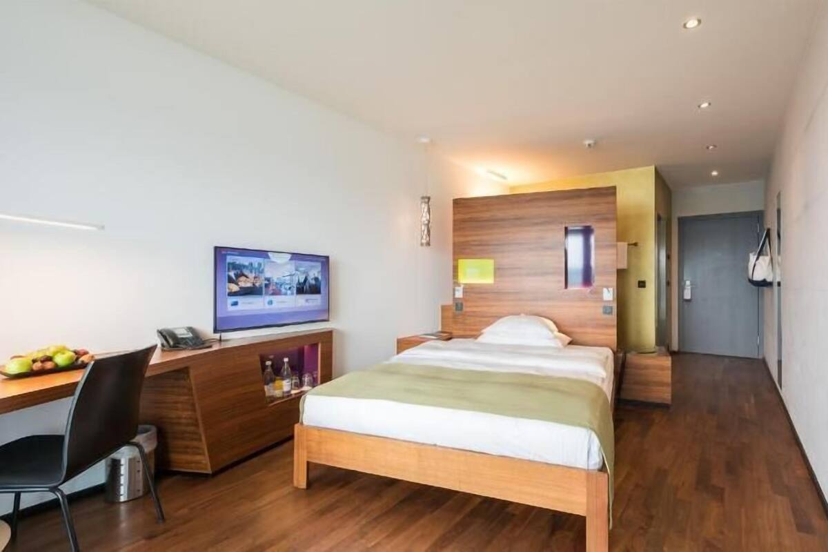 Ein modernes Hotelzimmer mit einem Holzbett, einem Schreibtisch mit Computer, einem Fernseher und einer kleinen Sitzecke.