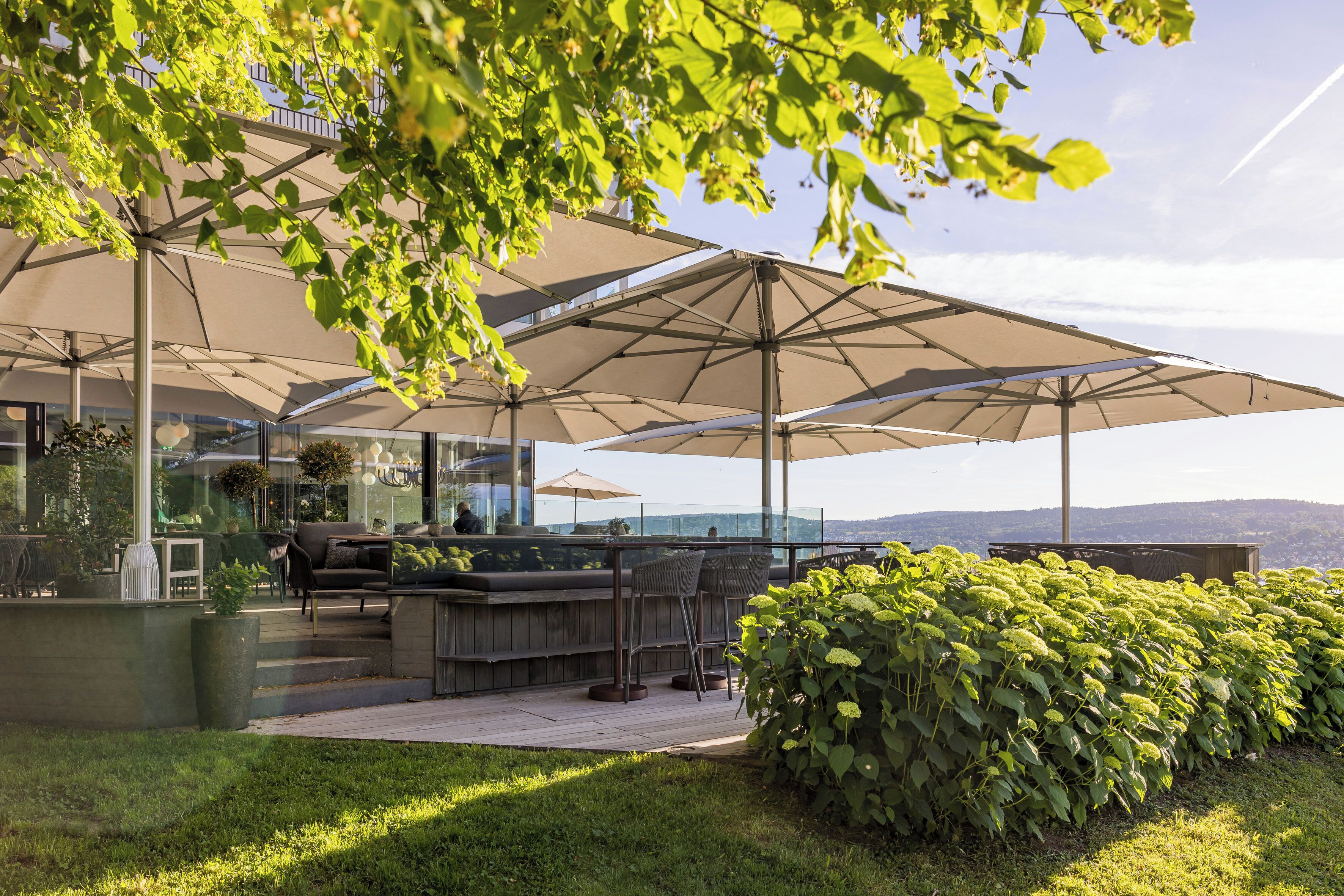 A modern outdoor seating area with large umbrellas, a bar, and a view of the landscape.