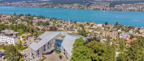 Un edificio moderno con fachada de vidrio, rodeado de casas residenciales y un lago.