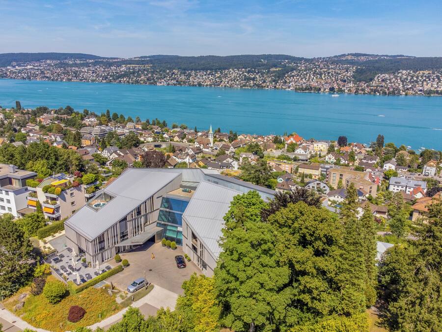 A modern building with a glass facade, surrounded by residential houses and a lake.