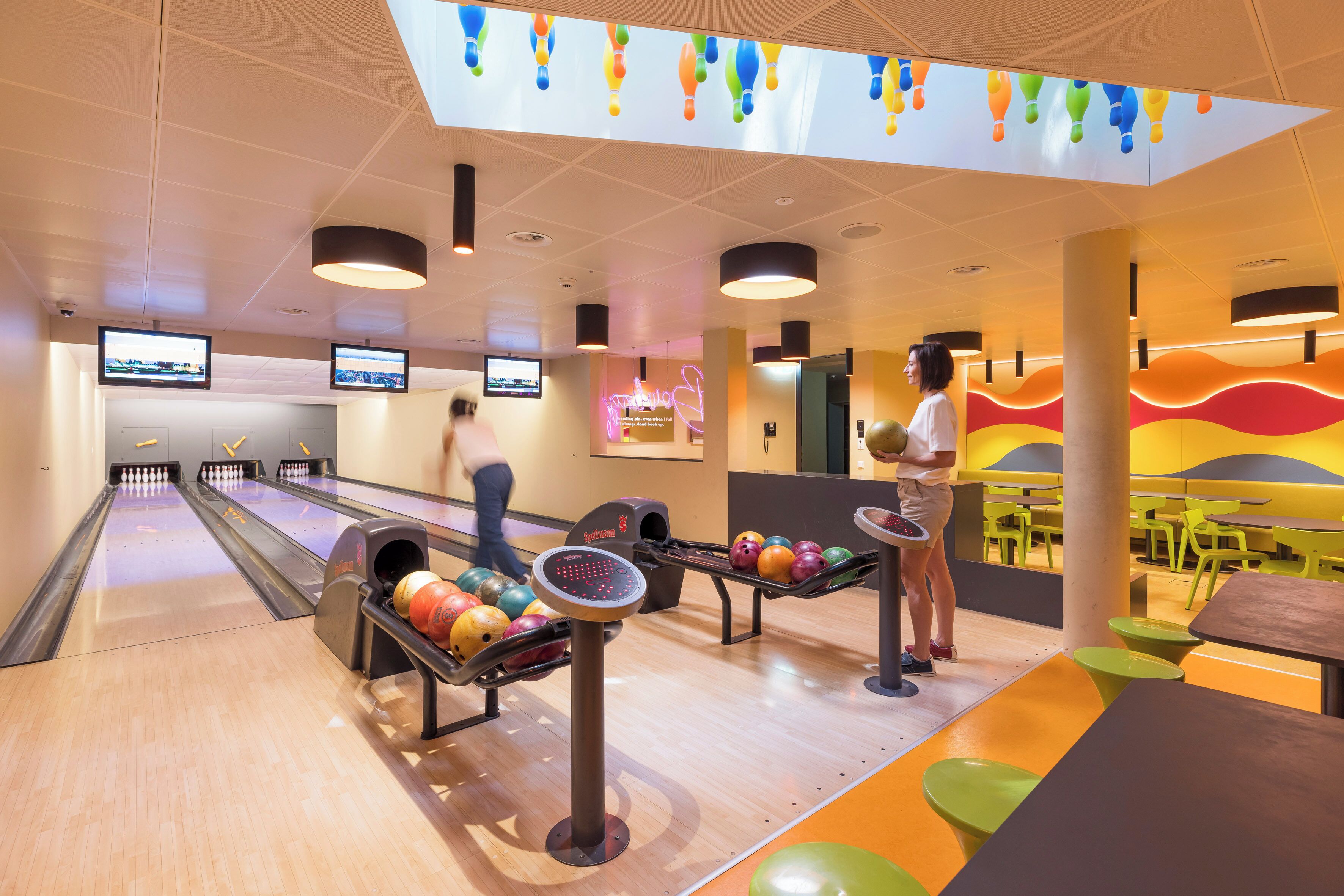 A bowling alley with multiple lanes, bowling balls, and a neon sign.