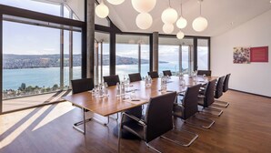 Ein Konferenzraum mit einem langen Tisch, Stühlen und großen Fenstern mit Blick auf ein Gewässer.