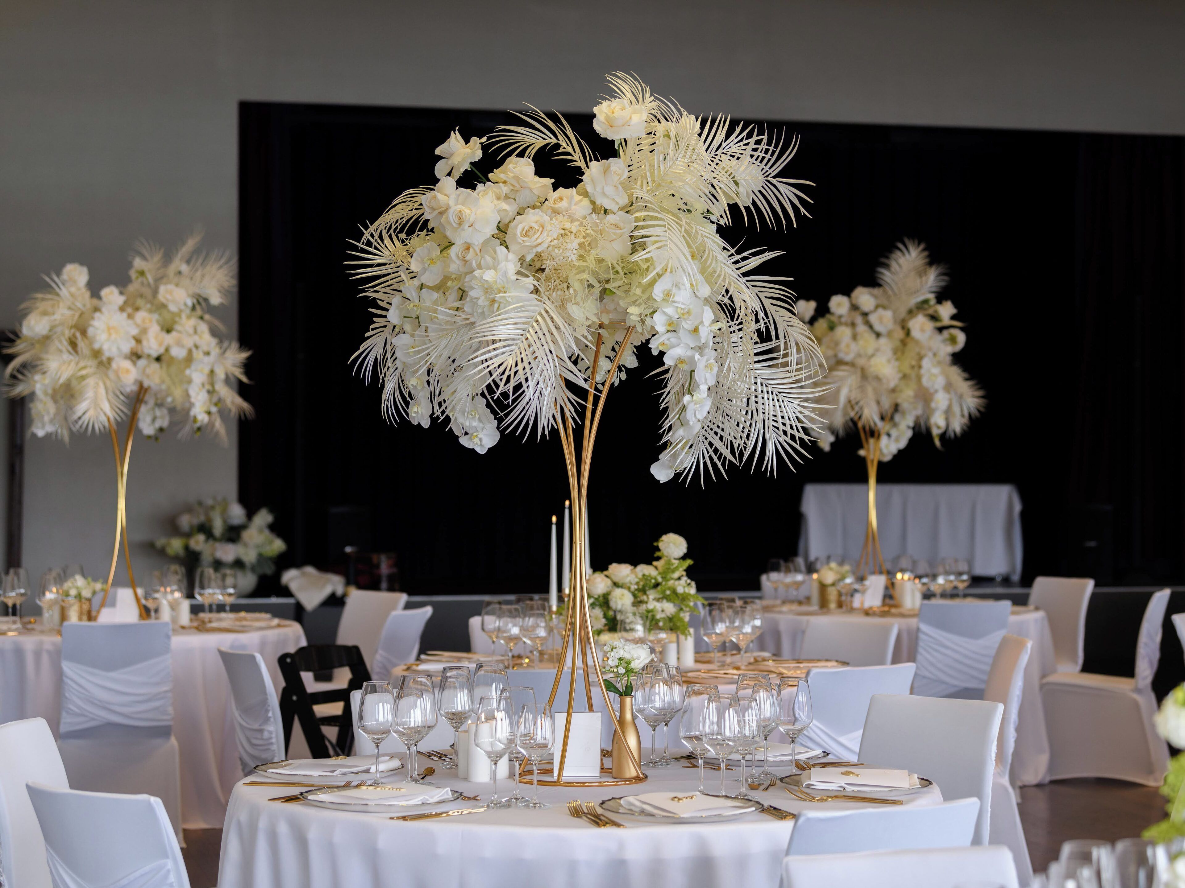 Un salón de banquetes con mesas redondas dispuestas para comer, con manteles blancos y detalles dorados.