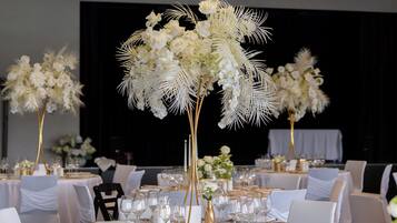Un salón de banquetes con mesas redondas dispuestas para comer, con manteles blancos y detalles dorados.