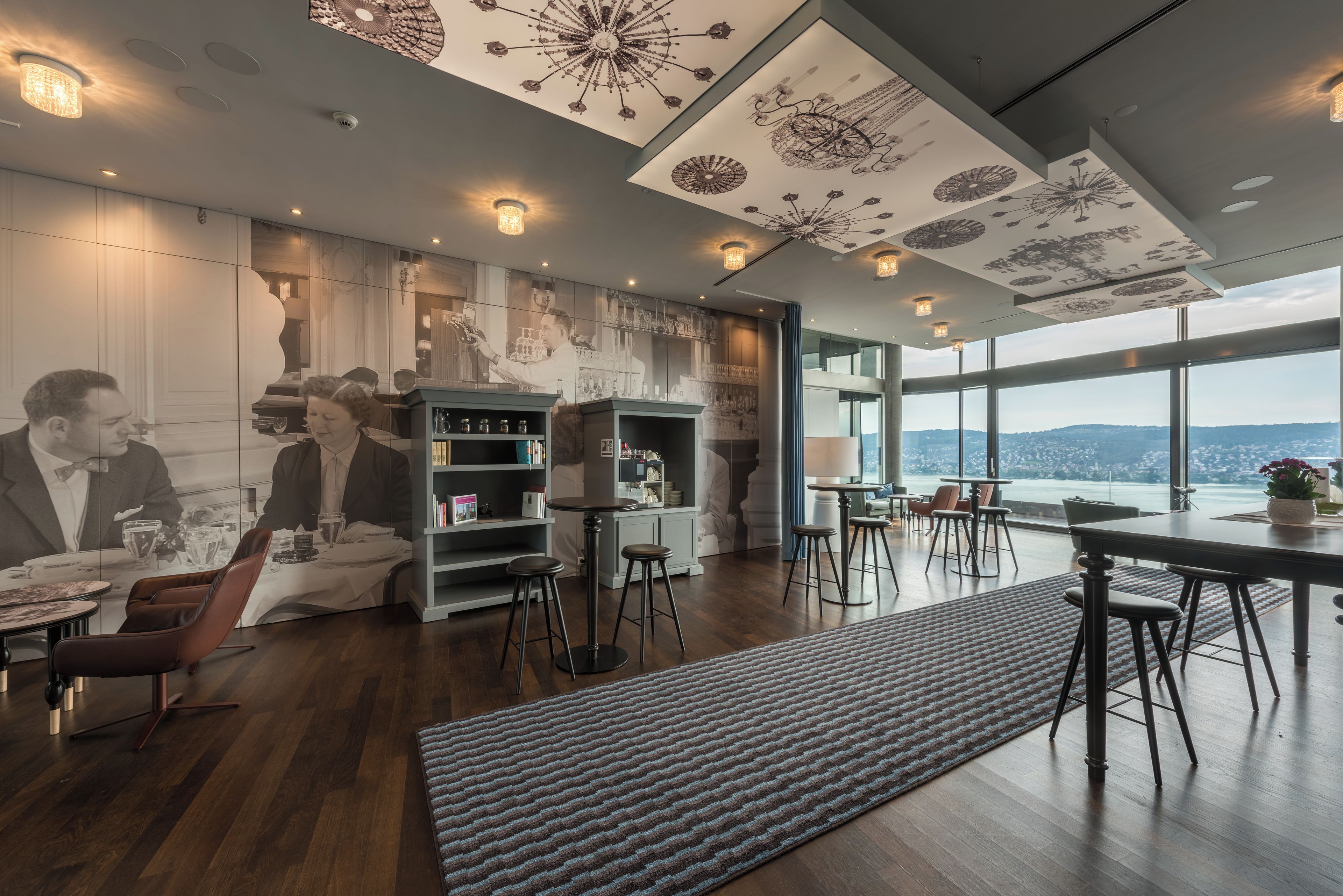 A modern interior with a bar area, high ceilings with decorative patterns, and a view of the city.