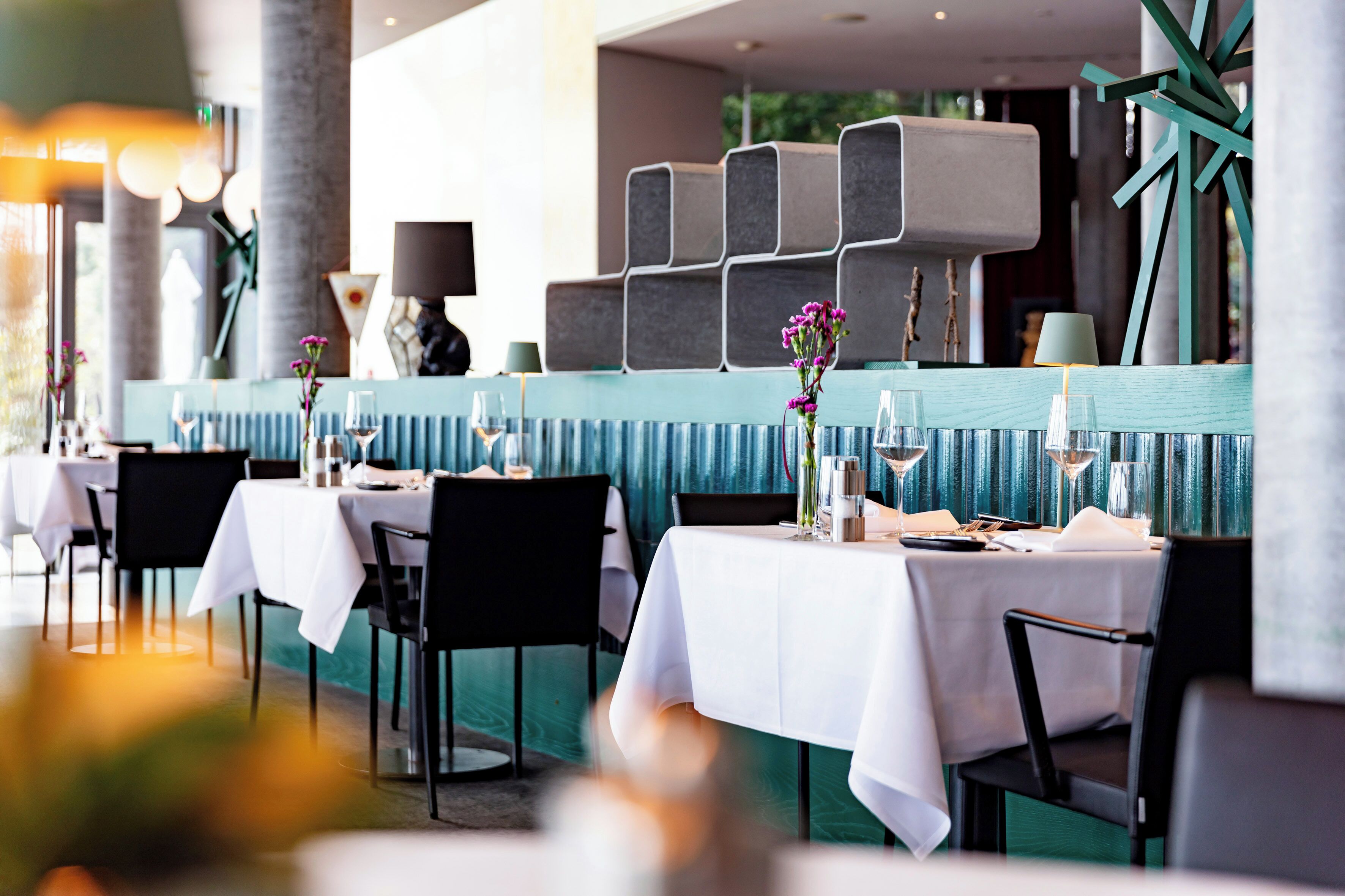 A restaurant with tables set for dining, featuring a modern design with teal accents and white tablecloths.