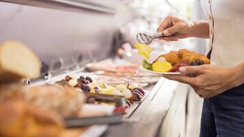 Une personne tenant une assiette remplie de différents aliments, notamment un croissant et des fruits, devant un buffet.