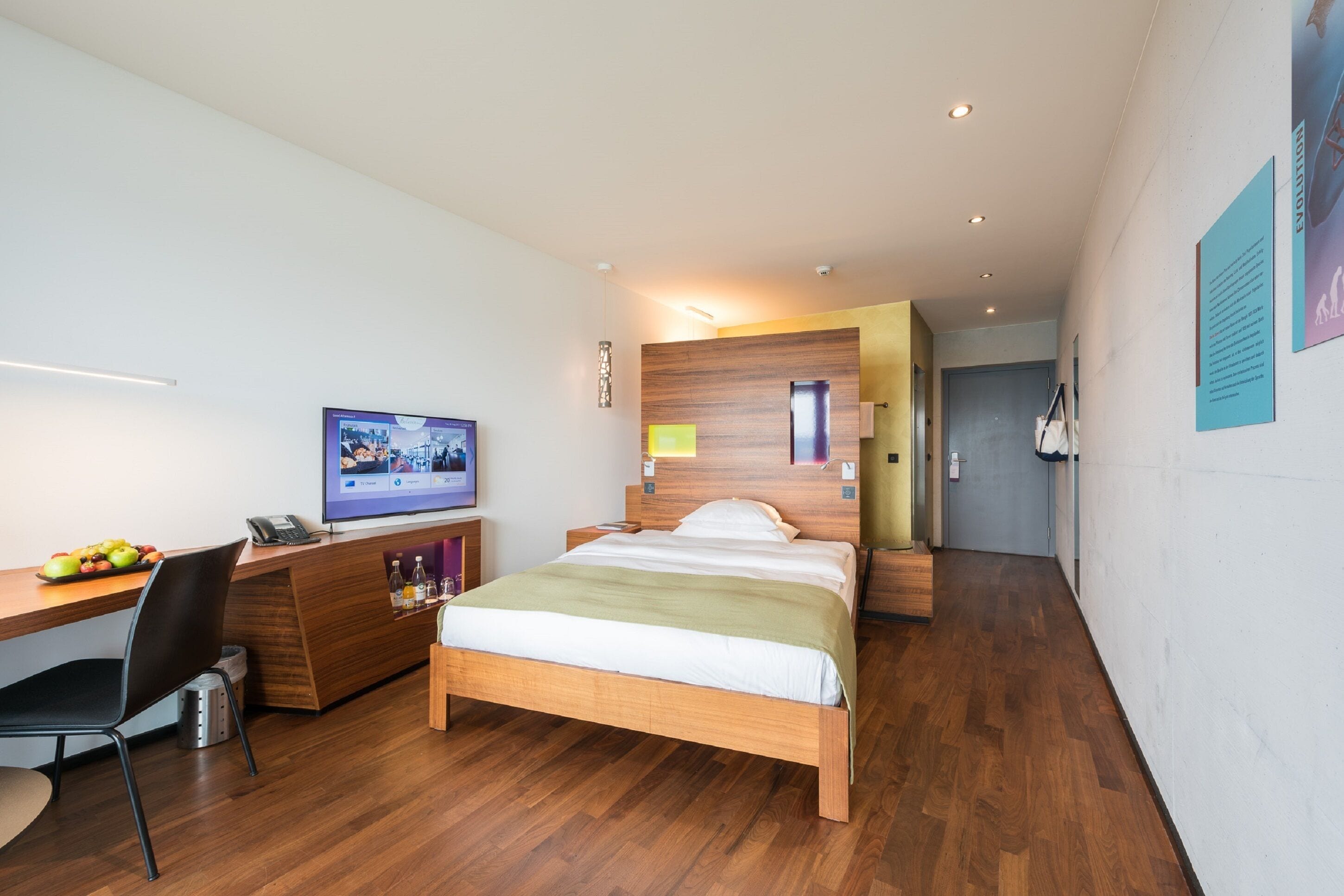 Une chambre d’hôtel moderne avec un lit en bois, un bureau avec un ordinateur, une chaise et un téléviseur.