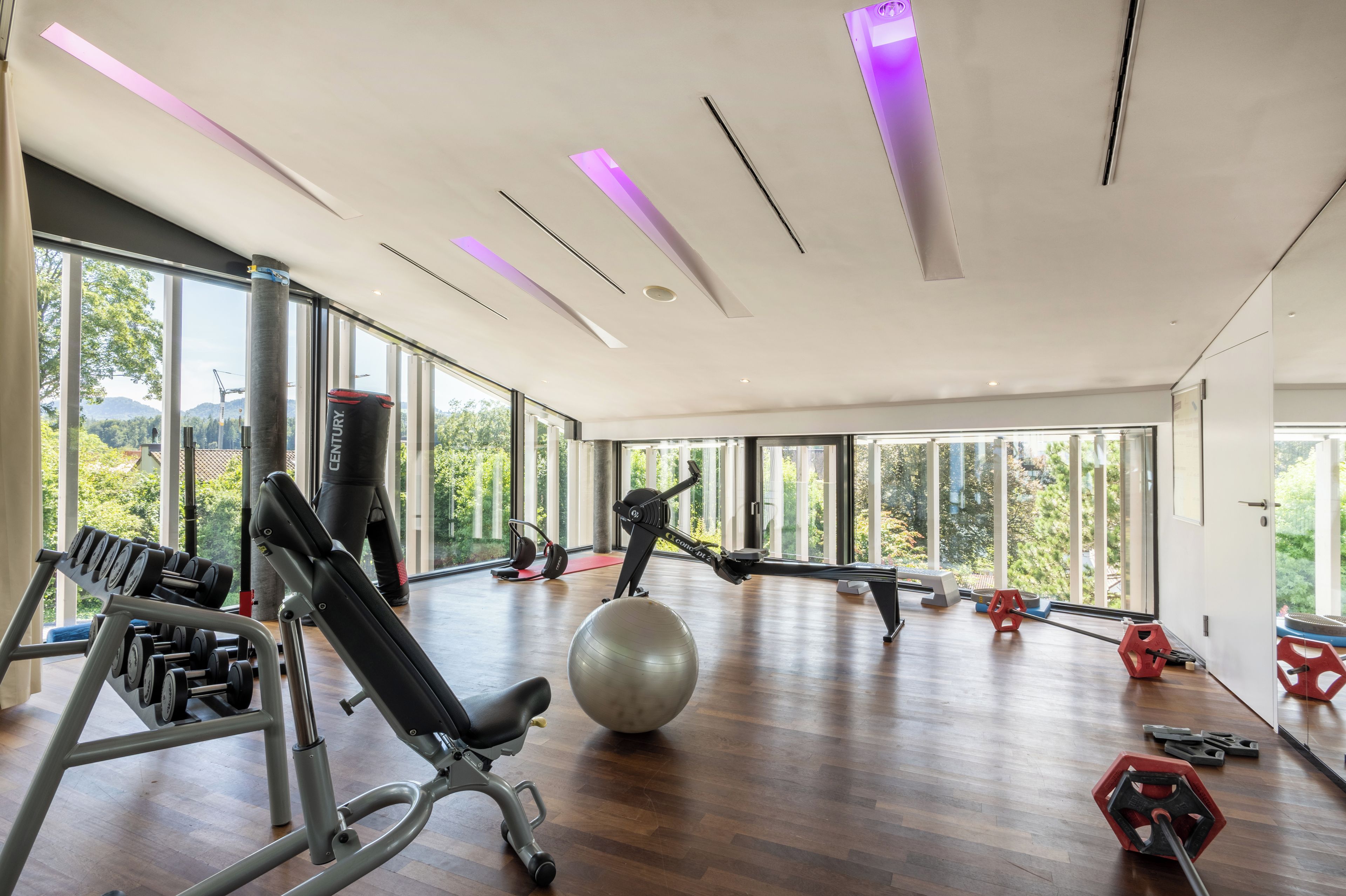 Un gimnasio espacioso con equipo de ejercicio, ventanas amplias y piso de madera.