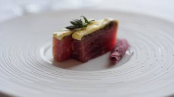 Une assiette contenant une tranche de viande recouverte d’une sauce crémeuse et agrémentée d’une branche d’herbe aromatique.