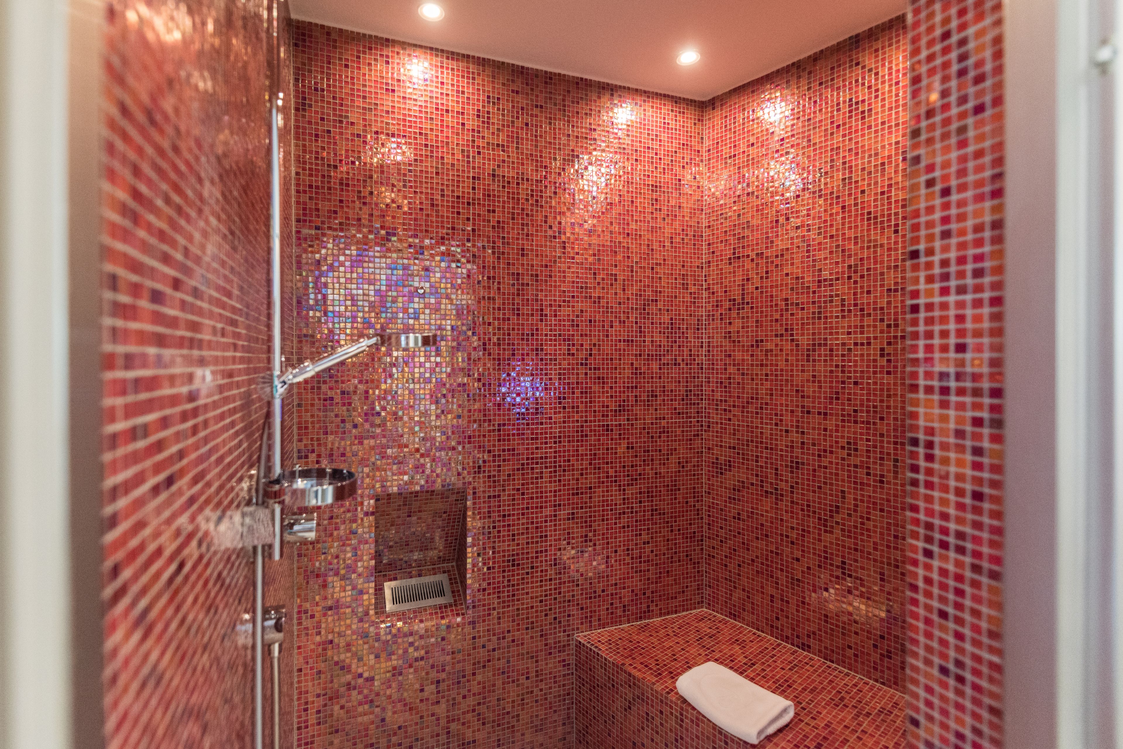 Ein Badezimmer mit Duschbereich, einer Sitzbank und einer gefliesten Wand.
