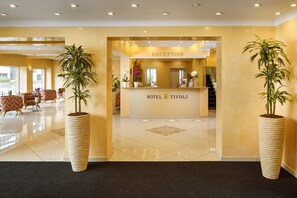 A hotel reception area with a reception desk, potted plants, and a staircase in the background. - Hotel Tivoli (Schlieren)