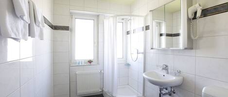 A modern bathroom with white tiles, a shower, a sink, and a mirror.