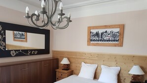A bedroom with a bed, wooden headboard, two bedside tables with lamps, a mirror, and a framed picture on the wall. - Hotel De Geneve (Geneva)