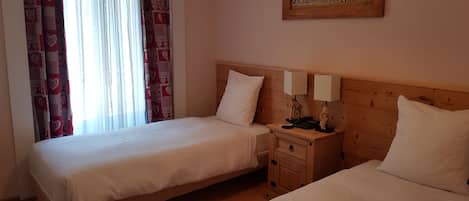 A hotel room with two single beds, a wooden headboard, a nightstand with a lamp, and a painting on the wall.