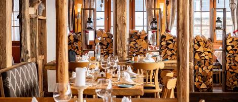 A restaurant with wooden beams, arched windows, and a long dining table set for a meal.