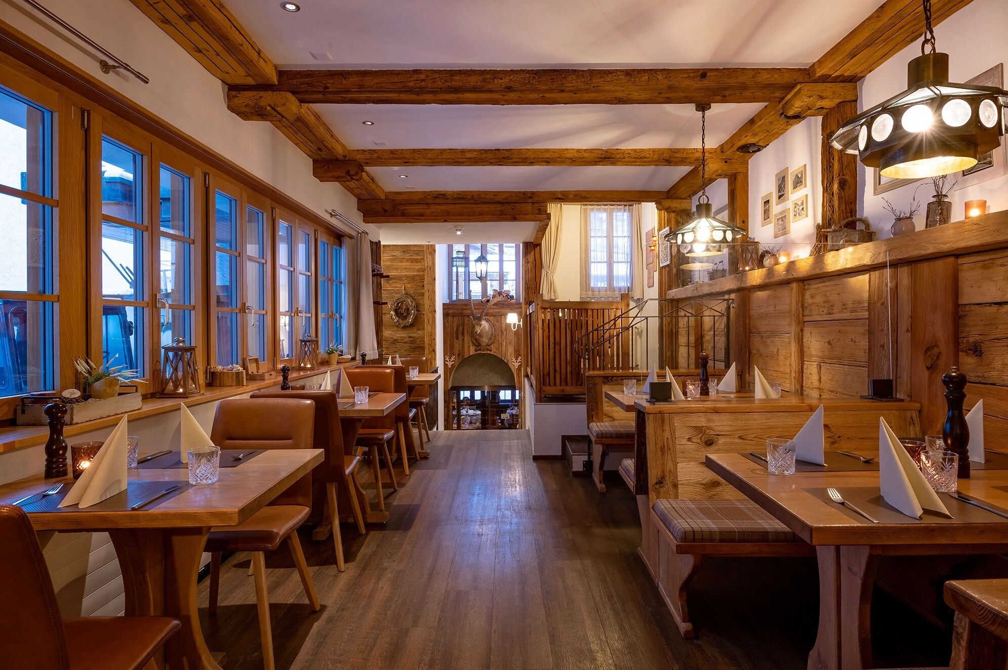 Un restaurant avec des poutres en bois, de grandes fenêtres et une arche centrale. Les tables sont dressées avec des couverts et des verres.