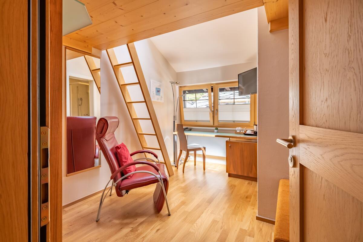 A compact room with a wooden ceiling, a red chair, a desk, and a window.