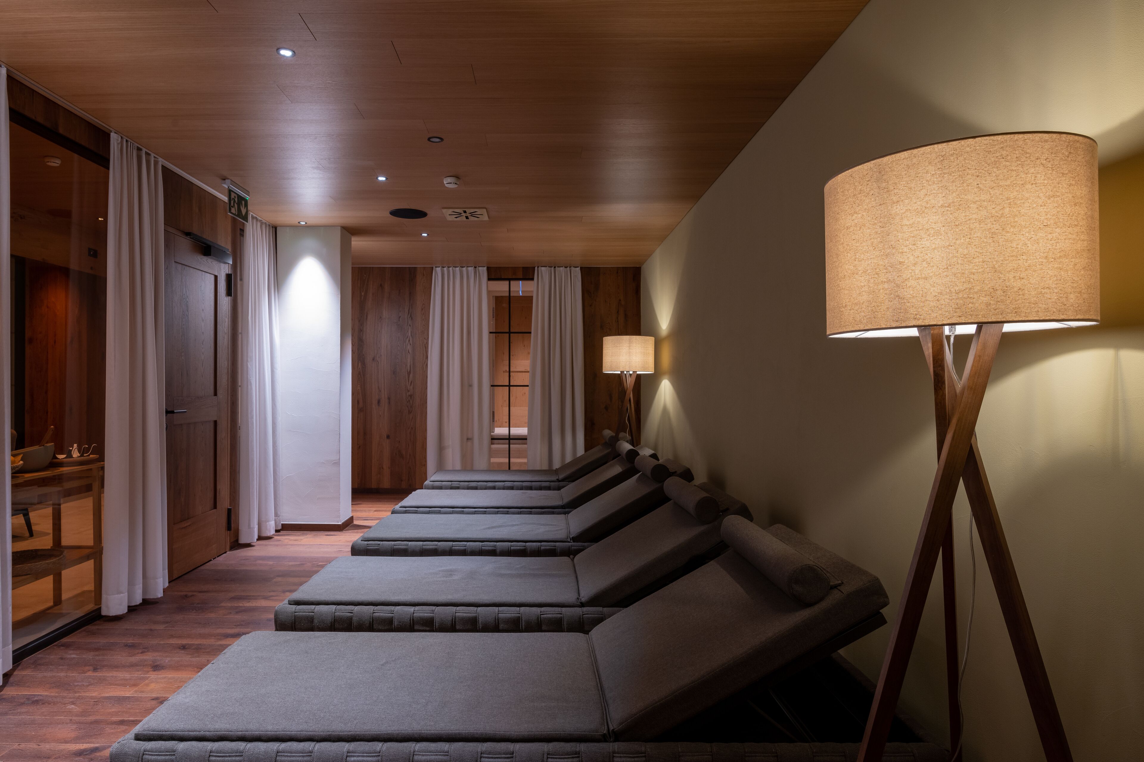 A spa room with wooden floors, a massage table, a standing lamp, and a door with a sign.