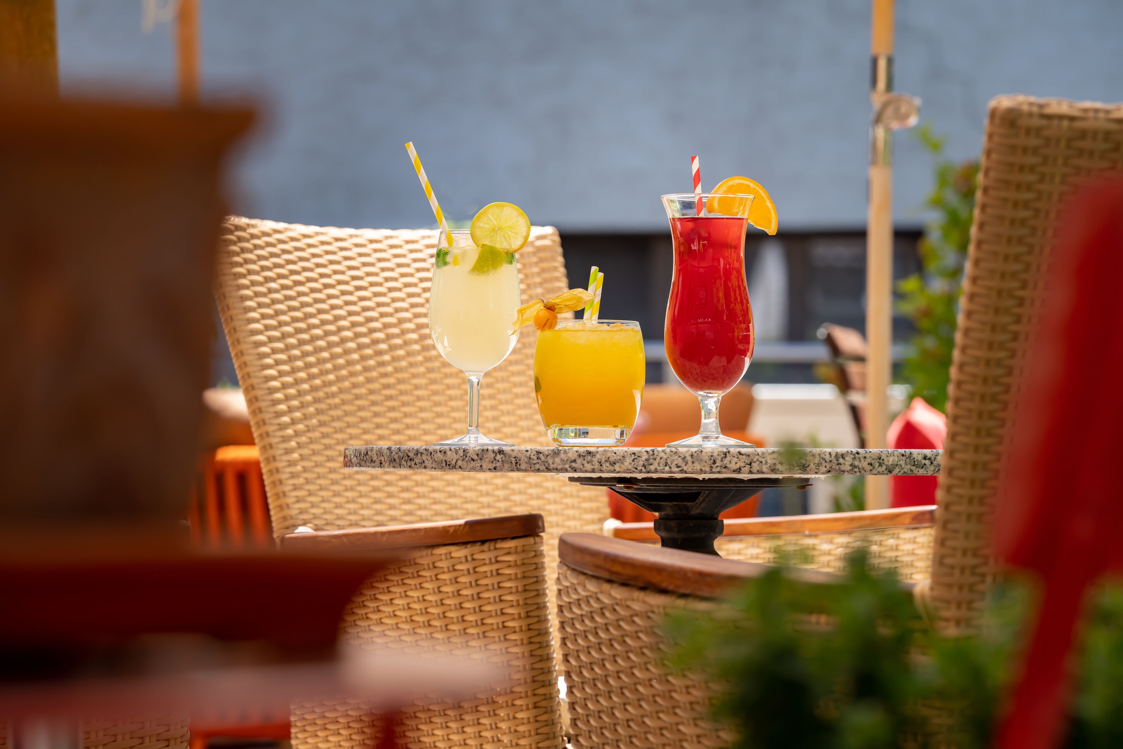 A table with three drinks, wicker chairs, and a view of the sea.