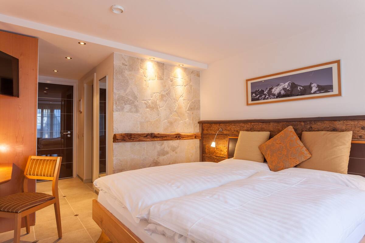A bedroom with a large bed, wooden headboard, and a stone accent wall.