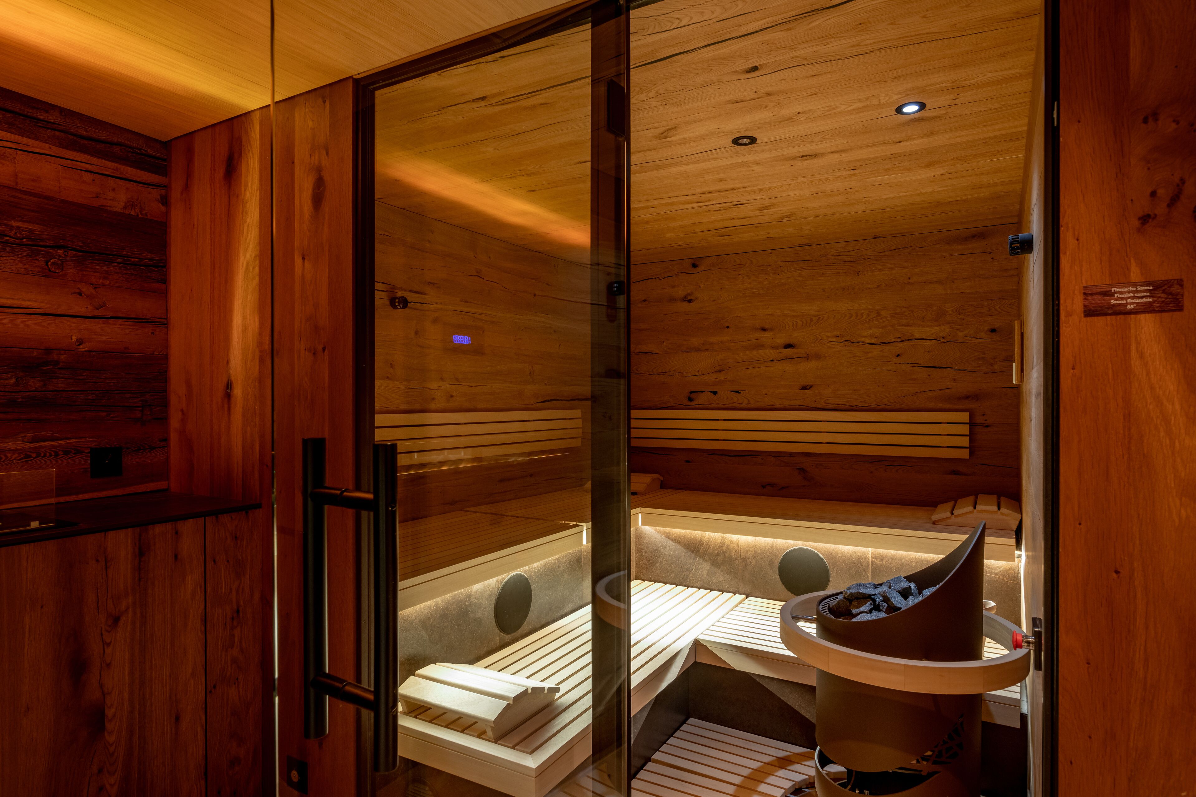 A wooden sauna with a glass door, wooden benches, and a stone basin.