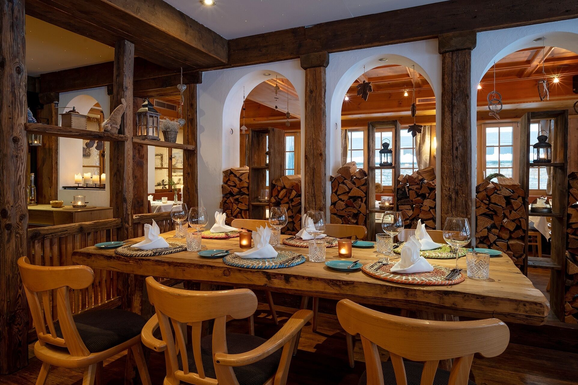 A dining area with wooden beams, arched windows, and a long table set for a meal.