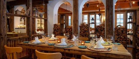 A dining area with wooden beams, arched windows, and a long table set for a meal.