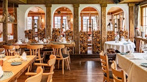 A restaurant with wooden tables and chairs, arched windows, and a rustic interior. - The Pollux (Zermatt)