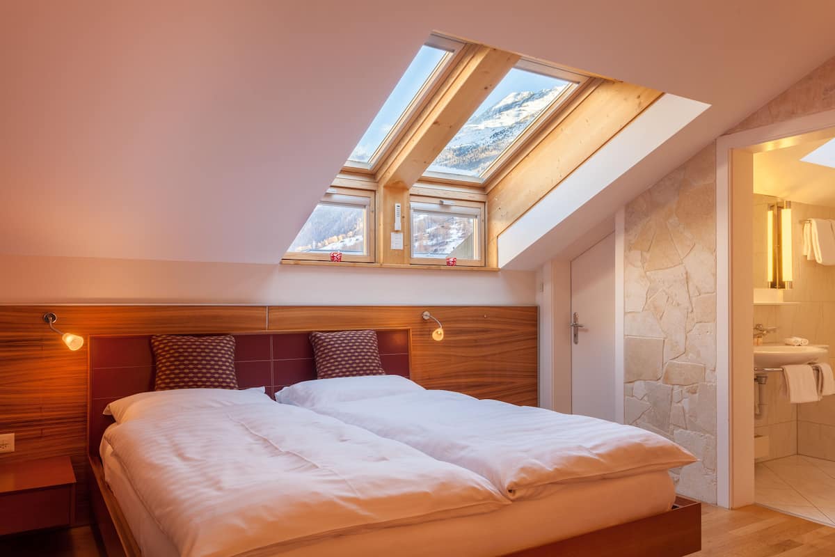 A bedroom with a skylight, a bed with white bedding, a wooden headboard, and a stone wall.