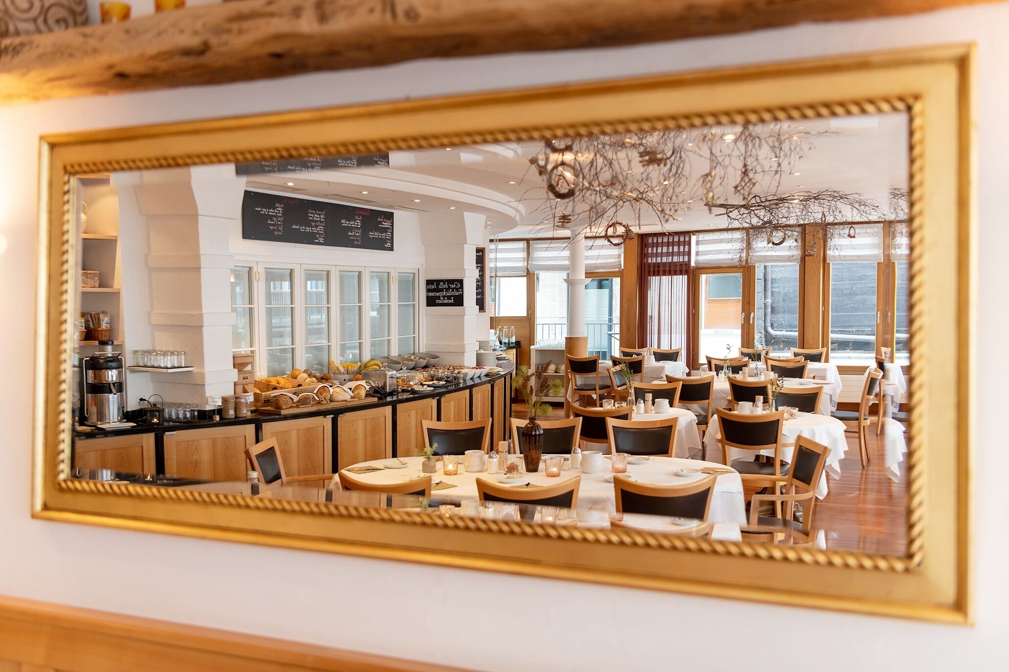 A restaurant with a mirrored wall reflecting the dining area, a counter with a coffee machine, and a menu board.