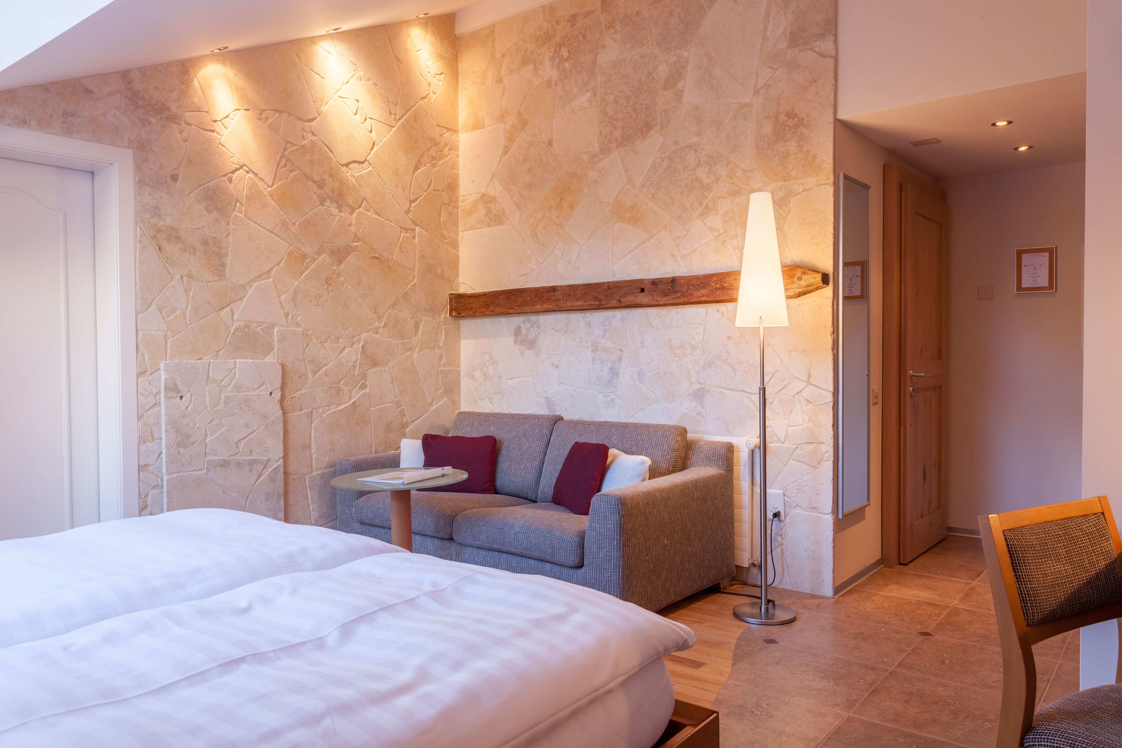 Habitació d'hotel moderna amb paret d'accent de pedra, un sofà, una taula de nit, una làmpada i una cadira.