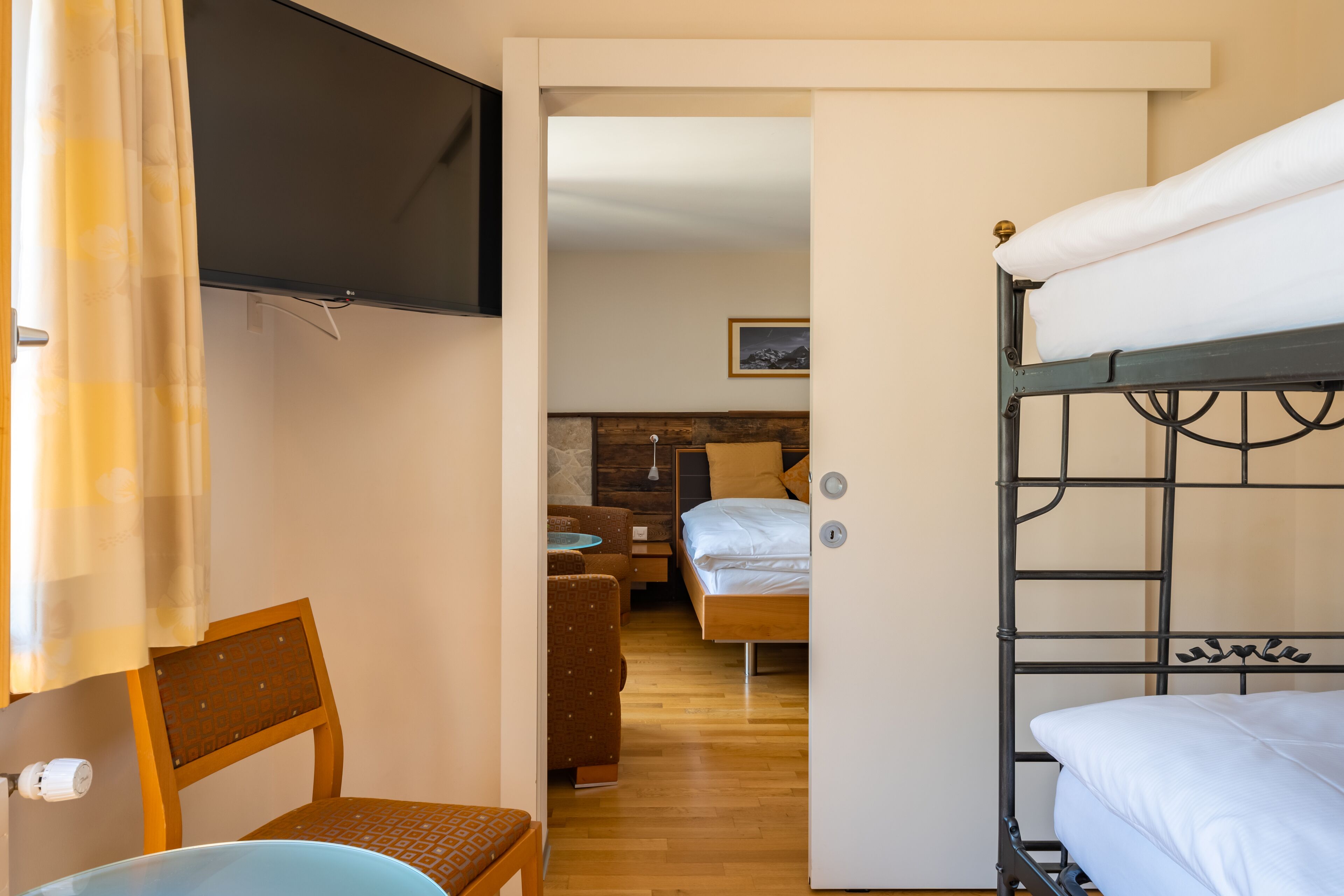 Ein Zimmer mit einem Etagenbett, einem Einzelbett, einem an der Wand montierten Fernseher, einem Holzstuhl und einem kleinen Tisch.