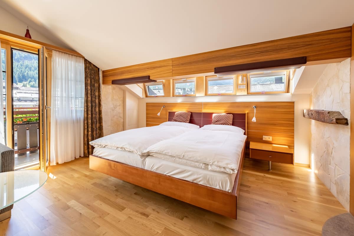 A modern bedroom with a large bed, wooden headboard, bedside tables, and a glass table.