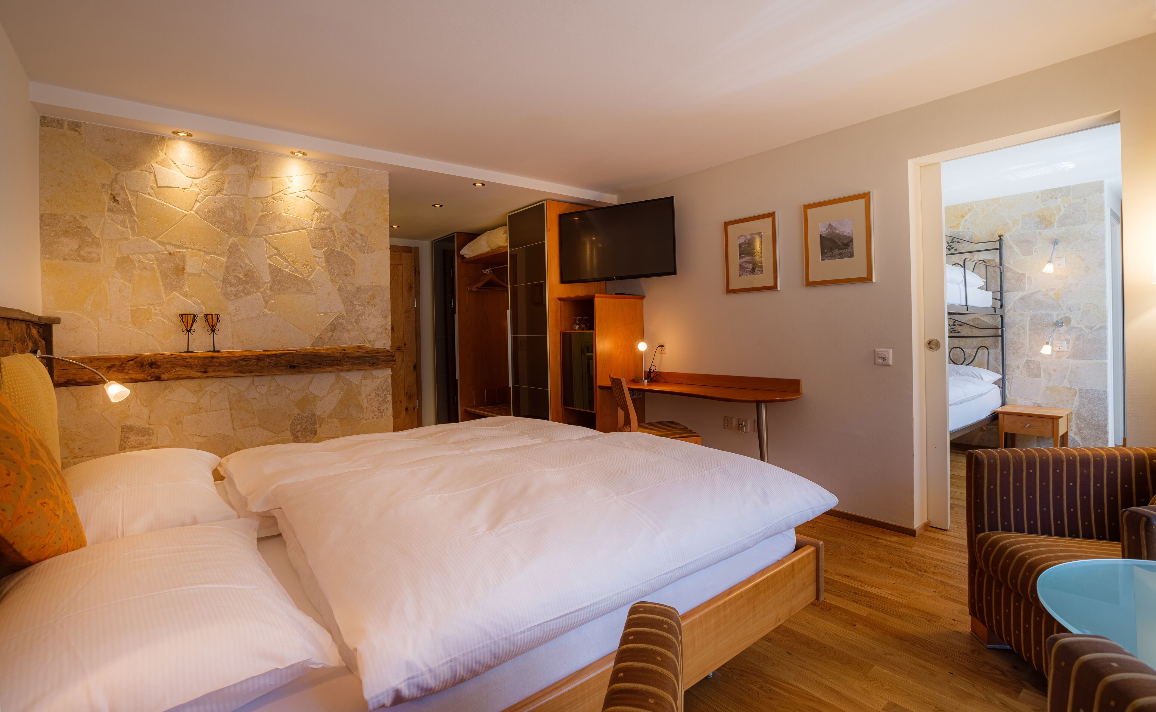 Un dormitorio con una cama grande, un escritorio, una silla, un televisor y una pared de piedra.