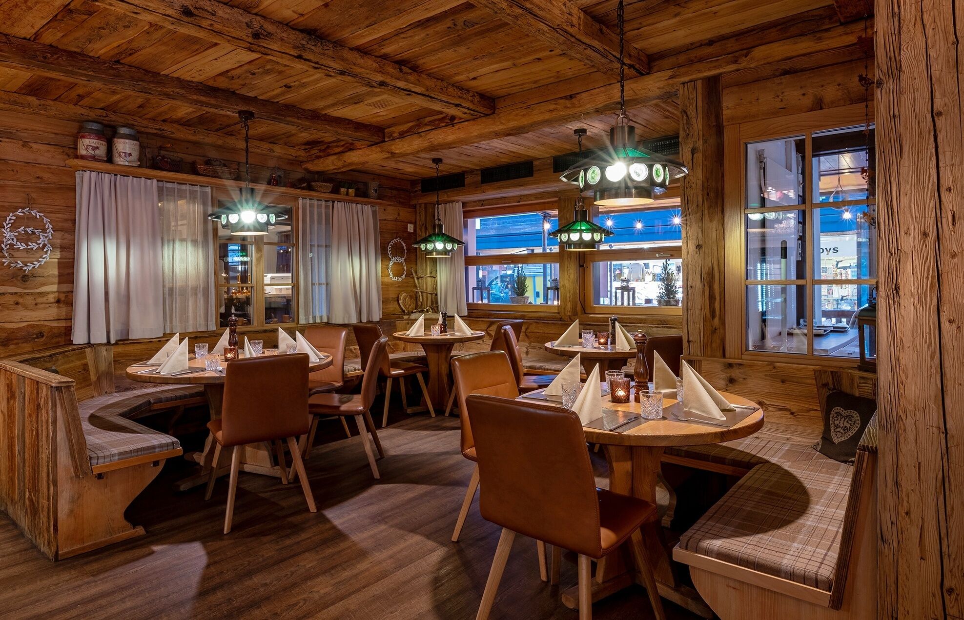 A cozy restaurant with wooden interiors, round tables, and leather seating.