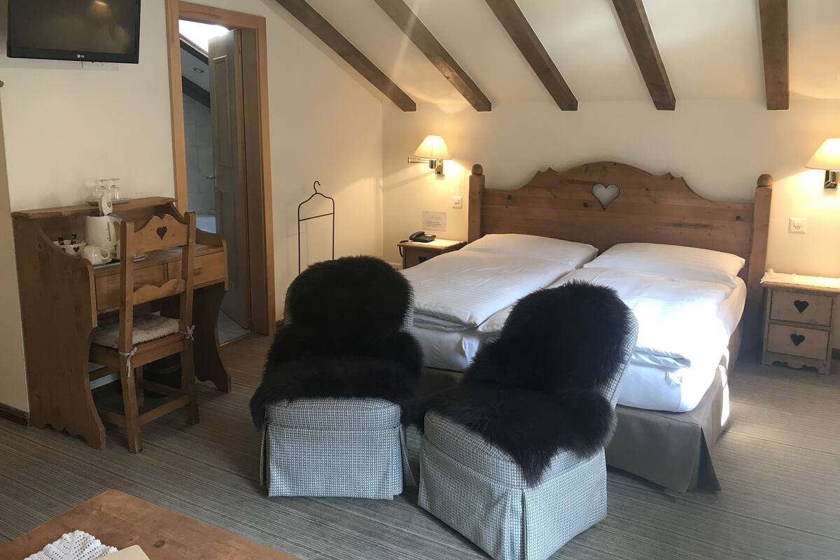 Ein Schlafzimmer mit Holz-Kopfteil, zwei Betten, einem Schreibtisch mit Stuhl, einem an der Wand montierten Fernseher und einer Pendelleuchte.
