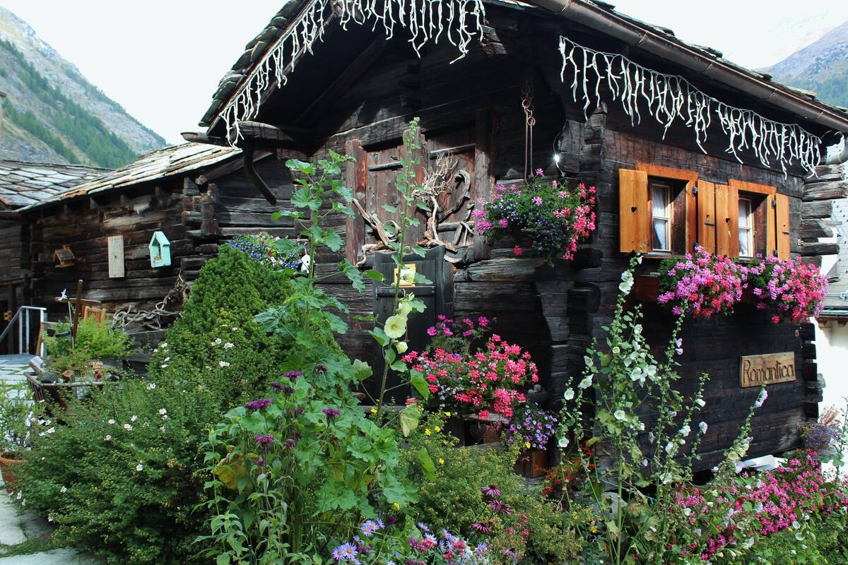Ein rustikales Holzhäuschen mit Balkon, geschmückt mit Blumen, und einem Schild mit der Aufschrift 'Romantik'.