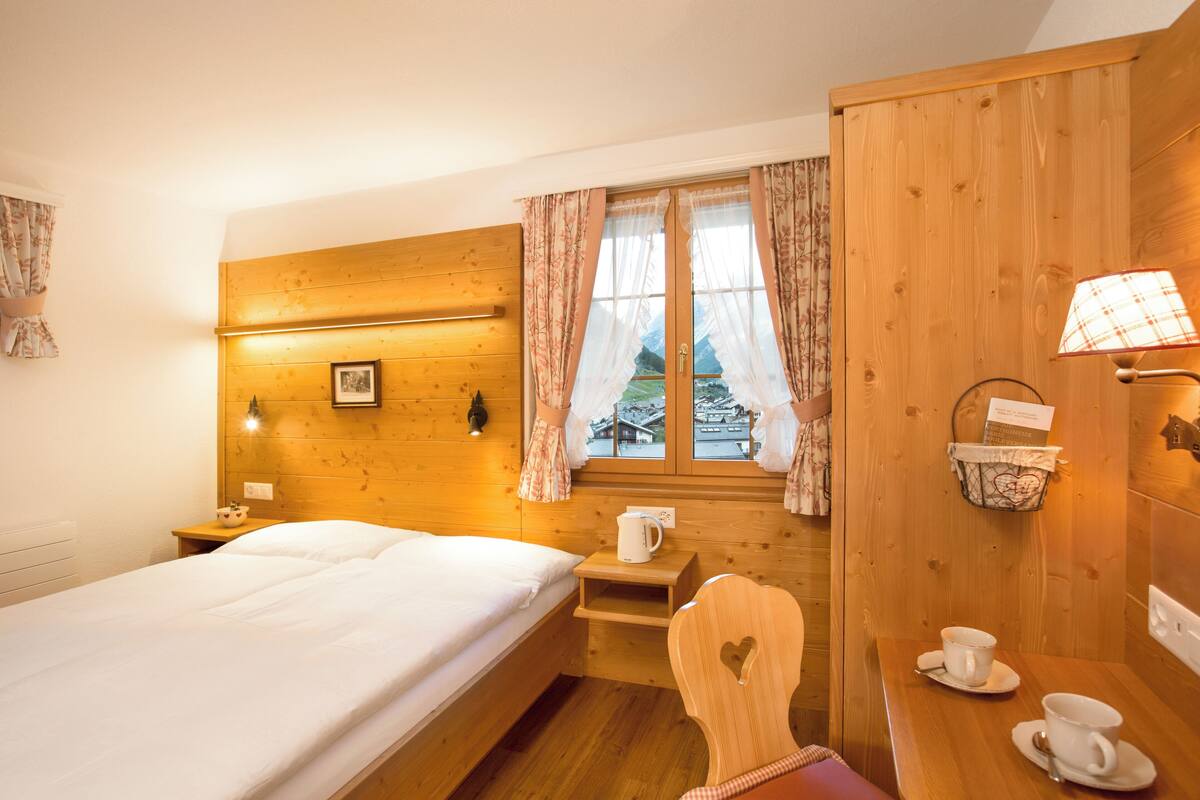 Ein gemütlicher Holzraum mit einem Bett, einem kleinen Tisch mit Tassen, einem Fenster mit Vorhängen und einer Lampe.