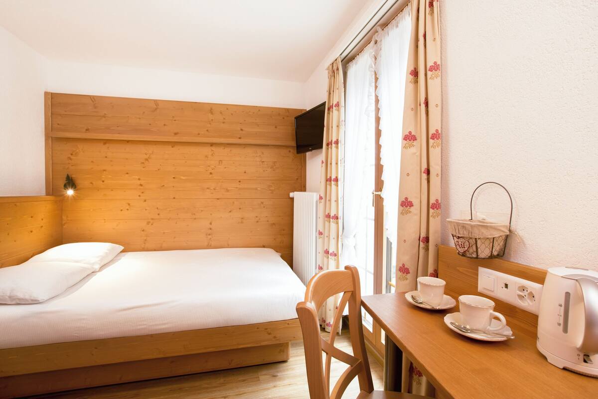 Ein hölzernes Bett mit weißer Matratze, ein Holztisch mit Wasserkocher, Tassen und einem Korb.